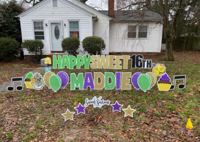 YL Hampton sign - "Happy Sweet 16th Maddie". Green, gold and purple letters (16th is black), Hogwarts crest, musical notes and cupcakes on front lawn in front of small white house.