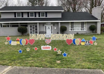 YL Hampton sign - "Happy Birthday" in gold glittery letters, surrounded by red, blue and gold cutout elements (hearts, balloons, cupcakes). "#1 Mom", "Celebrate".
