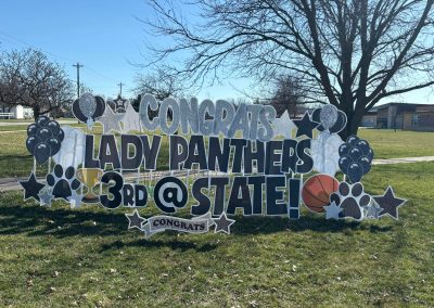 YL Northeast Boone sign - "Congrats Lady Panthers, 3rd @ State!". Sparkly silver + black letters surrounded by black and white balloon elements, glittery stars, pawprints , a basketball and trophy. In the background is a school building.