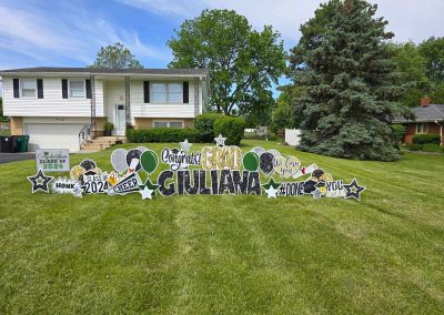 YL Expressions sign - "Congrats Grad Giuliana". Glittery gold and black letters surrounded by black, silver, gold and green elements (balloons, cheer, class of 2024).