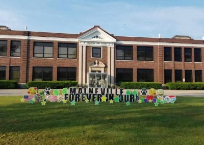 YL Little Miami sign - "Maineville Forever in Our Heart". Bold black text surrounded by yellow and green stars, emojis, school/art paraphernalia