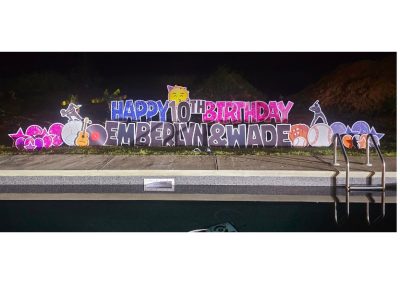 YL Emerals Coast sign - "Happy 10th Birthday Emberlynn & Wade". Glittery blue, pink and black letters surrounded by music and sports symbols for the girl and baseball symbols for the boy, as well as pink stars and balloons on her side and blue and orange on his.