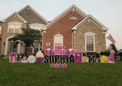 YL Little Miami sign - "Happy Birthday Sophia". Pink and black letters surrounded by magenta and purple birthday accents (cake, presents, balloons), horses, volleyball, "Kings Knights" logo.