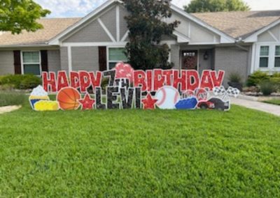 YL McKinney sign - "Happy 7th Birthday, Levi". Glittery red and black letters surrounded by cupcakes, stars, basketball, Lego, racecar and checkered flags.