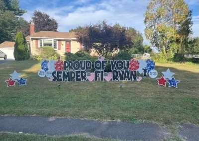 YL CT sign - "Proud of You, Semper Fi Ryan". Black letters surrounded by red, white and blue balloons and stars, patriotic accents