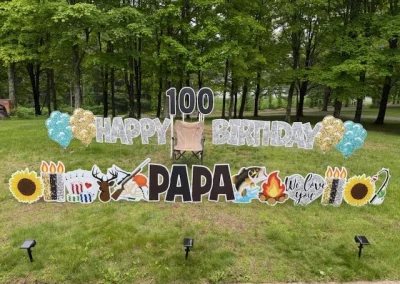 YL CT sign - "Happy 100th Birthday Papa". Glittery silver and black letters surrounded by gold and blue balloon accents, hunting and fishing symbolism, poker cards and chips, sunflowers