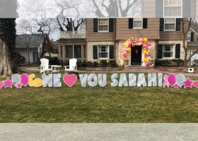 YL Kansas City sign - "We Heart You, Sarah!" Silver letters with a pink heart in the middle, breast cancer awareness symbolism, pink and silver balloons, hearts and stars